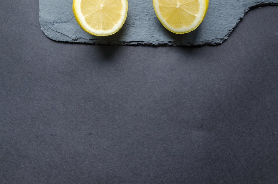 Close-up of fresh lemon halves on slate with a dark textured background.
